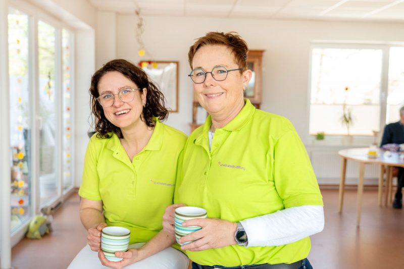 Zwei Frauen in St-Elisabeth-Poloshirts mit Kaffeetassen in der Hand